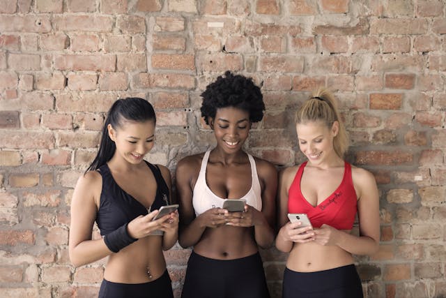 Três mulheres em fatos de treino a olhar para os seus telemóveis.