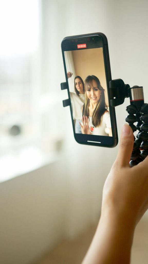 A female holding a tripod with a phone in it to film a vertical video of herself and a friend.