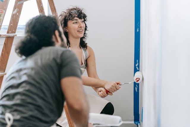 A man and woman painting a wall with a roller brush.