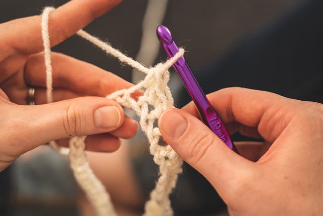 紫色のフックと白い毛糸でかぎ針編みをする人。