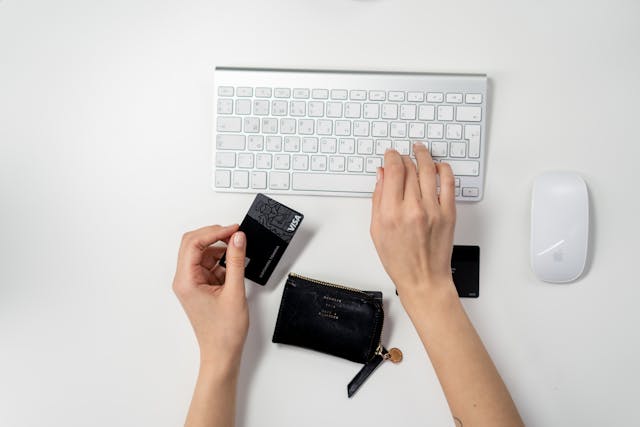 Someone typing on a keyboard while holding their credit card as they shop online.