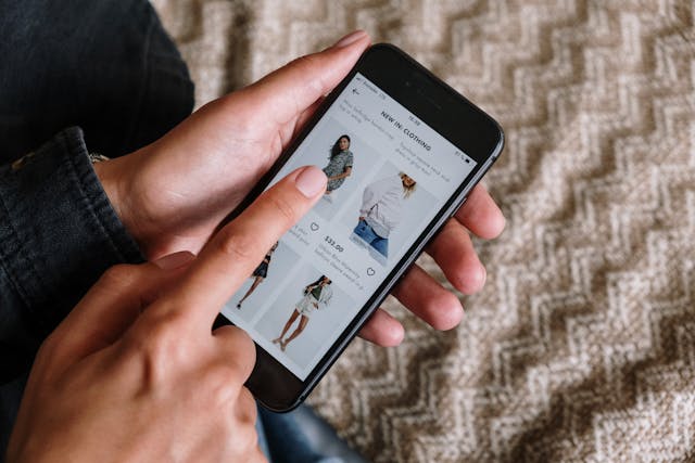 Cineva care se uită pe telefon la haine pe un site de cumpărături online și arată cu degetul spre unul dintre produse.