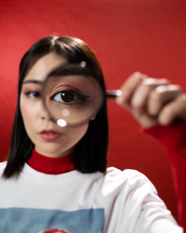 Een vrouw houdt een vergrootglas tegen haar oog.