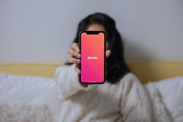 Une femme brandissant un téléphone affichant le logo de l'application Tinder.