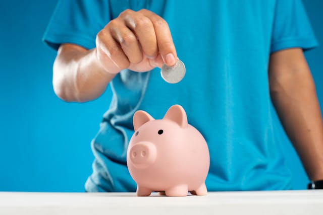 A man in a blue shirt putting a silver coin into a pink piggy bank