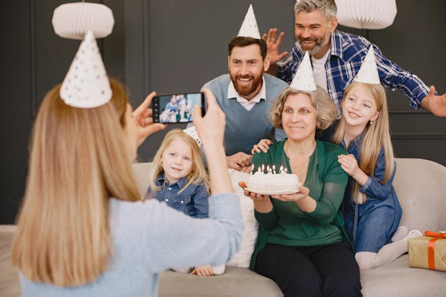 A woman taking a family photo at a birthday party with her phone.