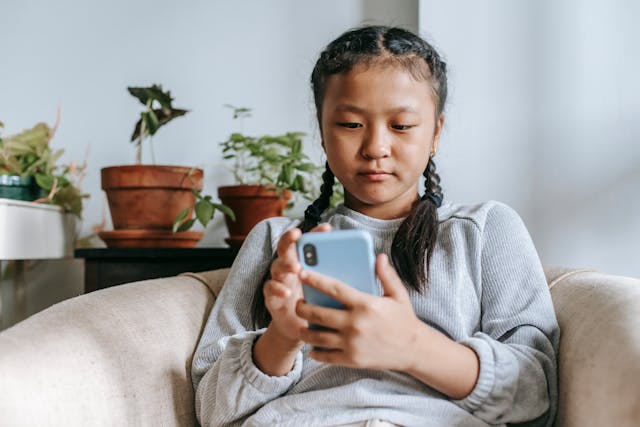 Een jong meisje doorzoekt haar blauwe mobiele telefoon. 