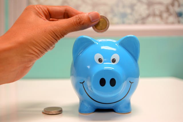 Someone dropping a coin into a blue piggy bank.