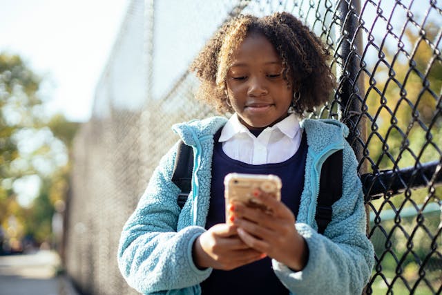 Eine junge Frau benutzt ihr Telefon, während sie sich an den Zaun lehnt.