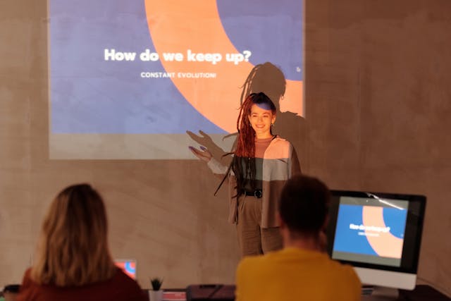 Een vrouw vooraan in een zaal die een presentatie geeft over de evolutie van sociale media.