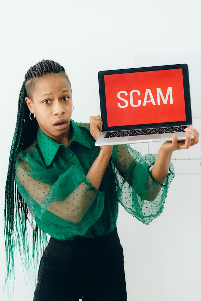 A woman holding up a laptop with the word “SCAM” on it.