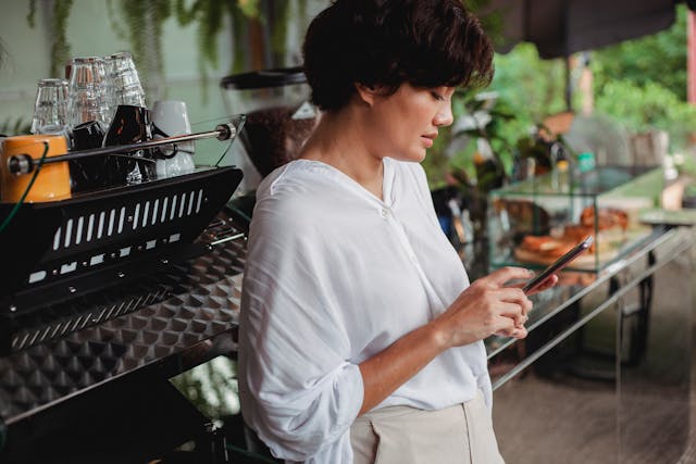 A woman leans on a counter while she scrolls her phone.