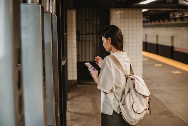 Vista trasera de una mujer utilizando su teléfono en una estación de metro. 