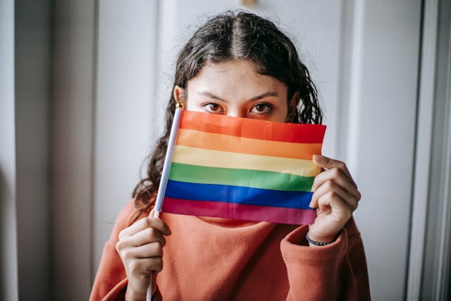 Una joven sostiene una bandera LGBT arco iris para cubrirse la mitad de la cara.