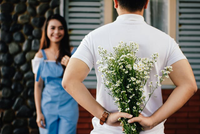 A man hiding baby’s breath flowers behind him as he walks up to a woman.