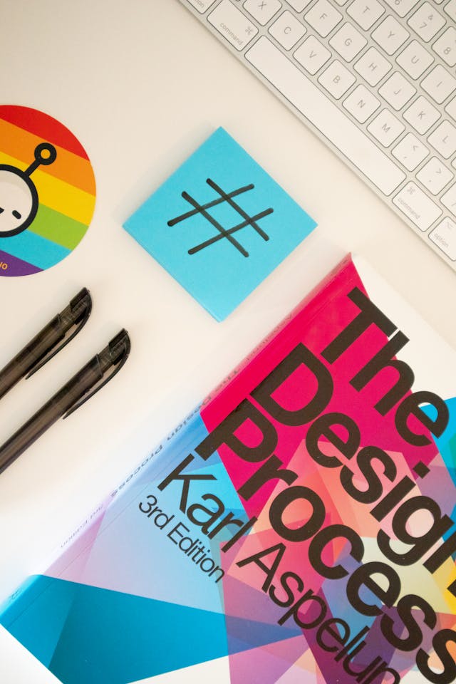 Een sticky note met het hashtagsymbool naast een designboek, een toetsenbord en pennen.