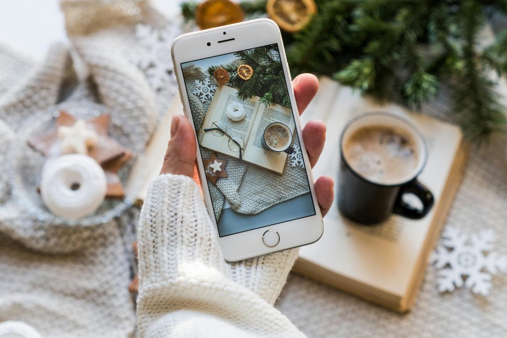 Someone taking a meticulously arranged flat-lay photo of a book and coffee with their phone to post on Instagram.