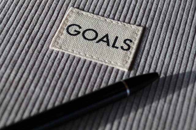 A pen lying on top of a notebook with the word “GOALS” on its cover.