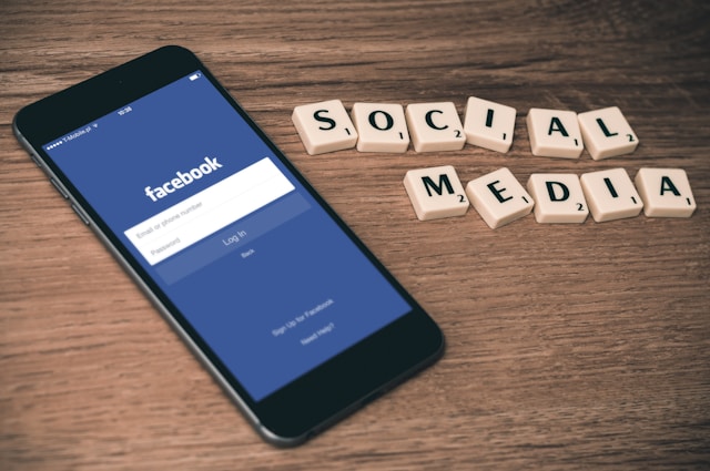 Un telefon cu ecranul de autentificare pe Facebook alături de piese de Scrabble pe care scrie "Social Media"