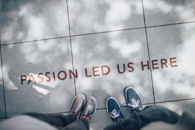 Zwei Personen stehen auf einem gefliesten Boden, auf dem die Worte "Passion led us here" stehen.