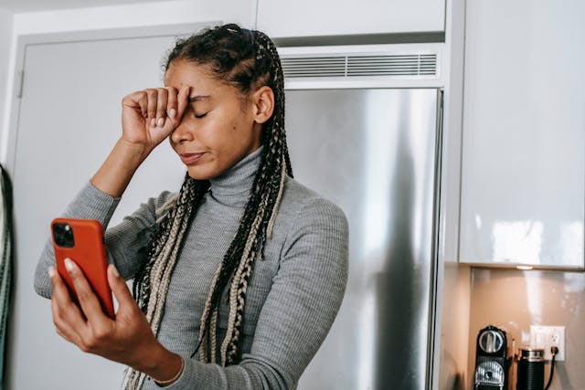 Een gefrustreerde vrouw houdt haar vuist tegen haar hoofd terwijl ze scrollt op Instagram op haar telefoon.