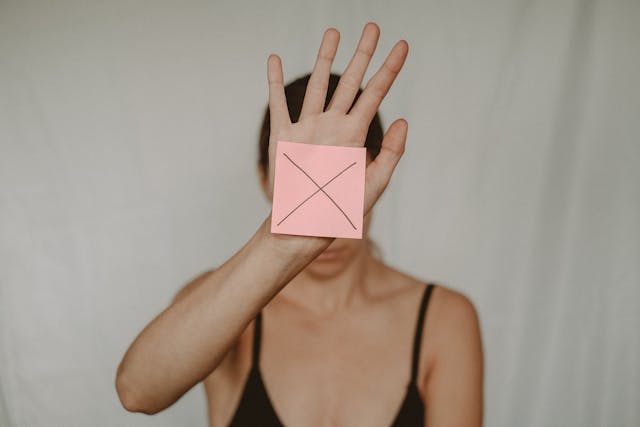 A woman holding up her hand, where a sticky note with an “X” mark is stuck on her palm.