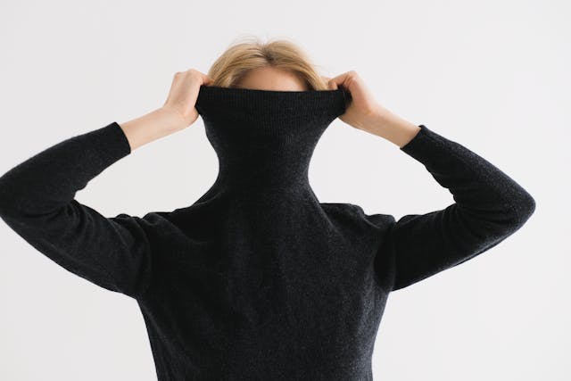 一個女人把她的黑色毛衣拉到頭上，以隱藏她的身份。