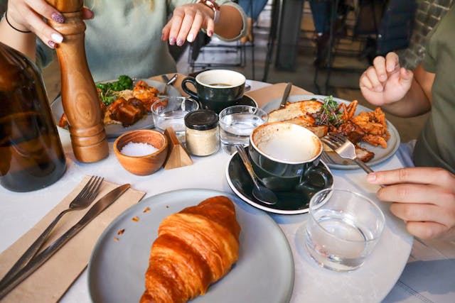 Duas pessoas num restaurante com comida de brunch, croissants e café na mesa.