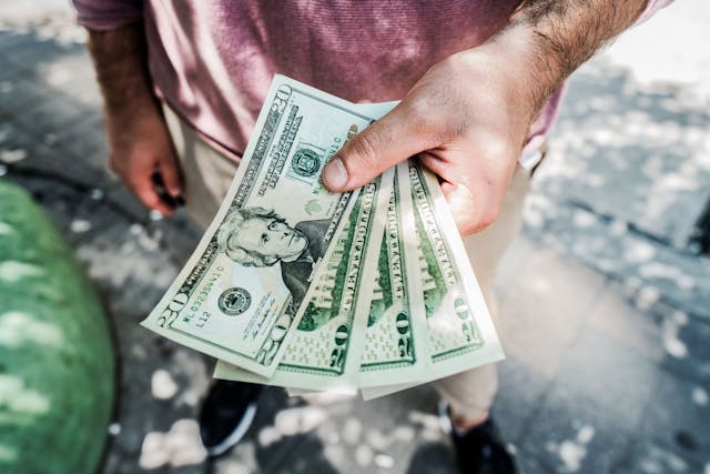 Un homme tenant un éventail de quatre billets de vingt dollars.