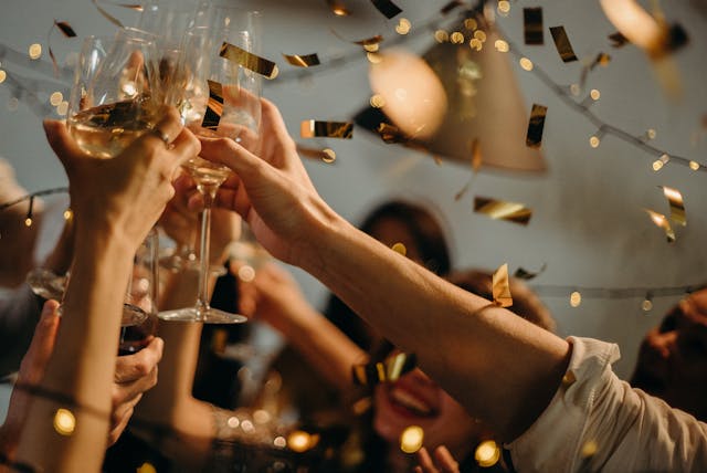 Gente chocando copas de champán para brindar en una fiesta con confeti a su alrededor.