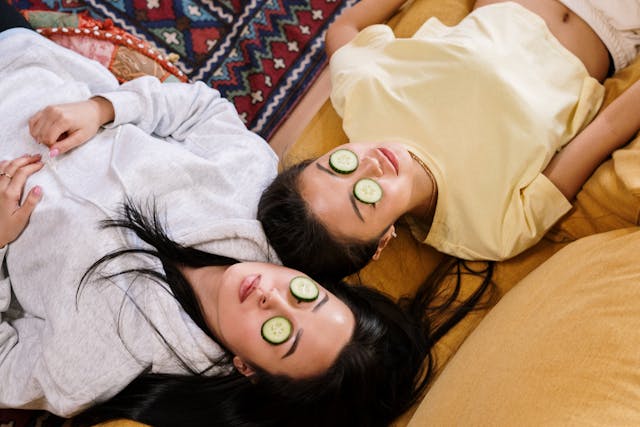 Two women relaxing and lying down with cucumber slices over their eyes.