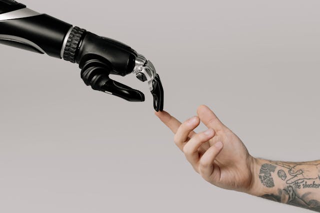 A robotic hand and a human hand touching fingertips.