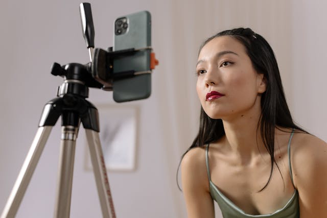 한 여성 인플루언서가 스마트폰과 삼각대를 사용하여 자신의 얼굴을 클로즈업하여 촬영하고 있습니다.