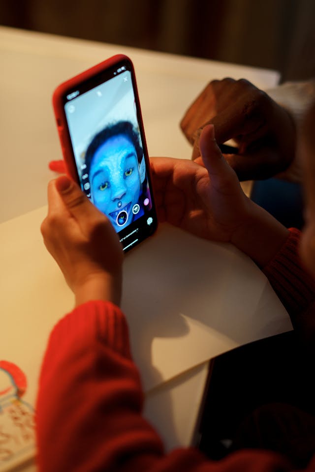 A child looking at her face with an Avatar AR filter through a phone’s front cam.