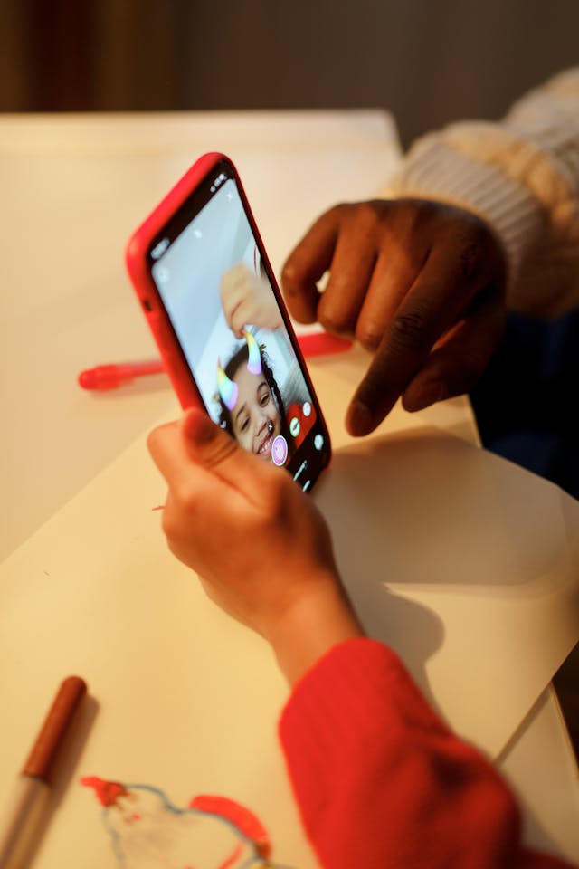 Une petite fille sourit en se voyant avec des cornes AR sur la tête sur la caméra frontale d'un téléphone.