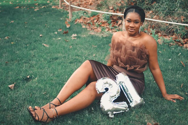 "21"이라고 적힌 풍선을 들고 잔디밭에서 포즈를 취하는 한 여성.