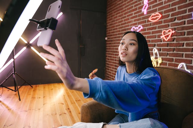 A woman setting up a live stream session with fans on her phone while holding a slice of pizza.