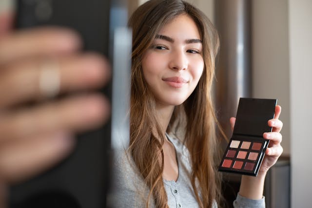 A female creator holding her phone up as she films a video of herself talking about a makeup palette.