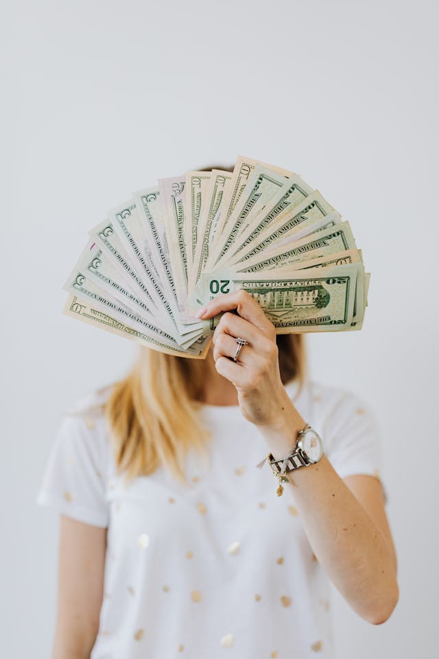 A woman holding a fan of US dollar bills to cover her face.