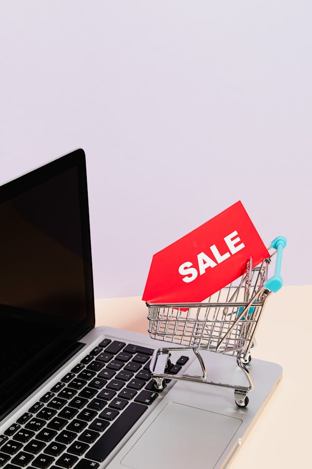 A miniature shopping cart with a sale tag inside on top of a laptop.