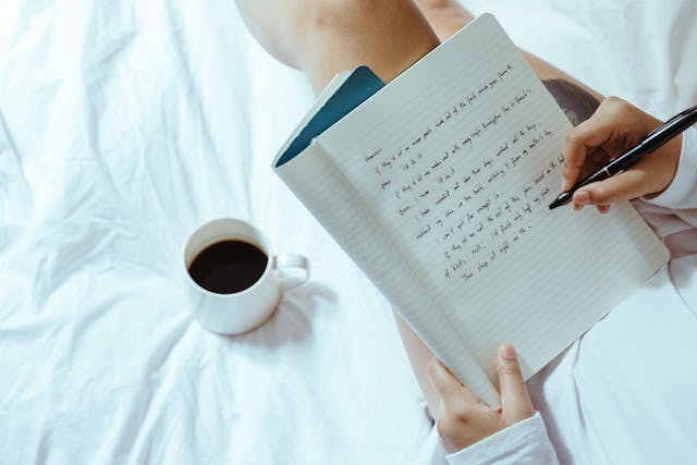 Someone writing in a notebook while having coffee in bed.