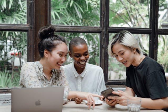 Three friends smiling and laughing while watching something on a phone.