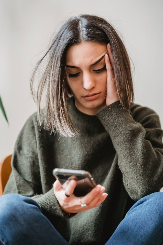 An upset woman with her hand on her face looking at her smartphone.