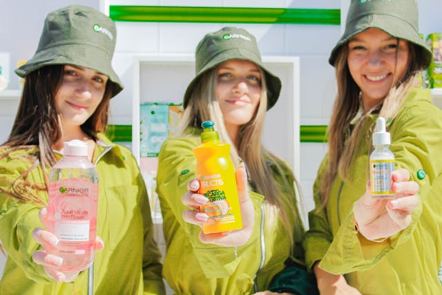Tres mujeres jóvenes sonríen a la cámara mientras sostienen productos de belleza.