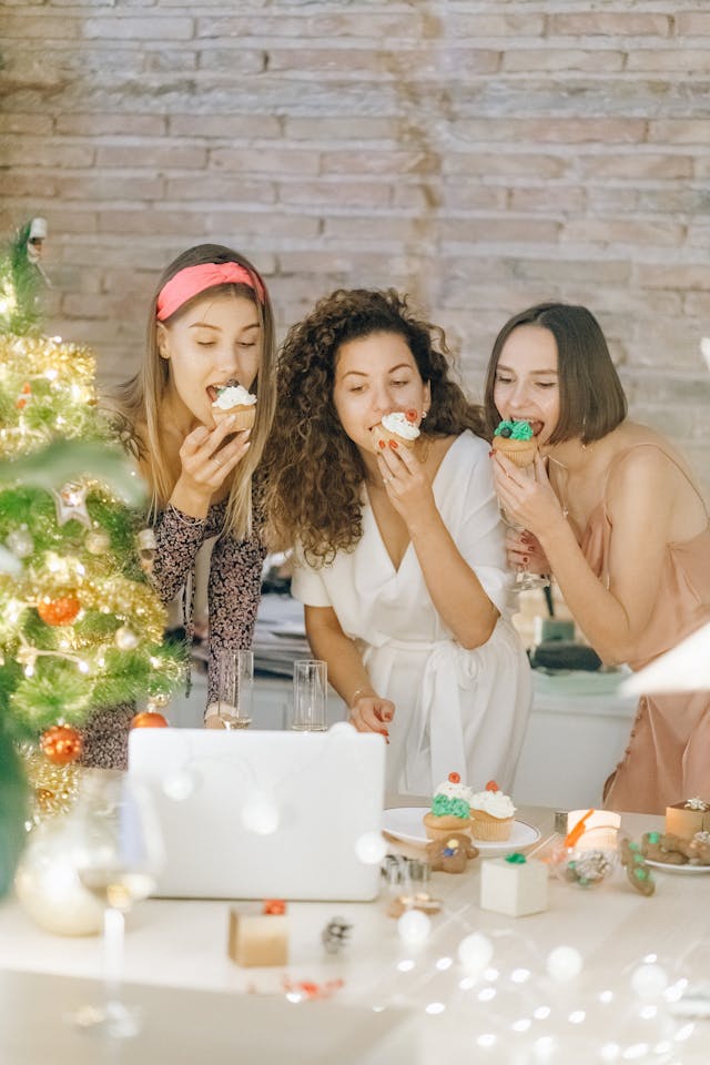 ثلاث نساء يأكلن الكعك أثناء تسجيل مقطع فيديو لأنفسهن على جهاز كمبيوتر محمول.
