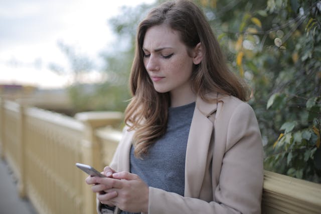 Een vrouw met gefronste wenkbrauwen die naar haar telefoon kijkt.