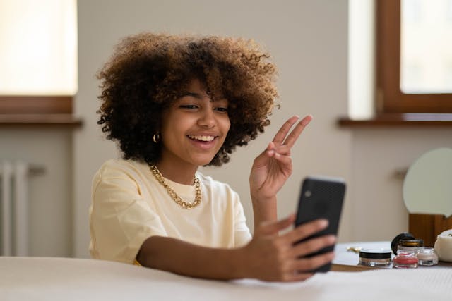 A micro-influencer holding up a peace sign while talking to her followers on a live stream on her phone.