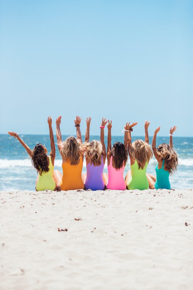 六位穿著五顏六色泳衣的女人並排坐在沙灘上。