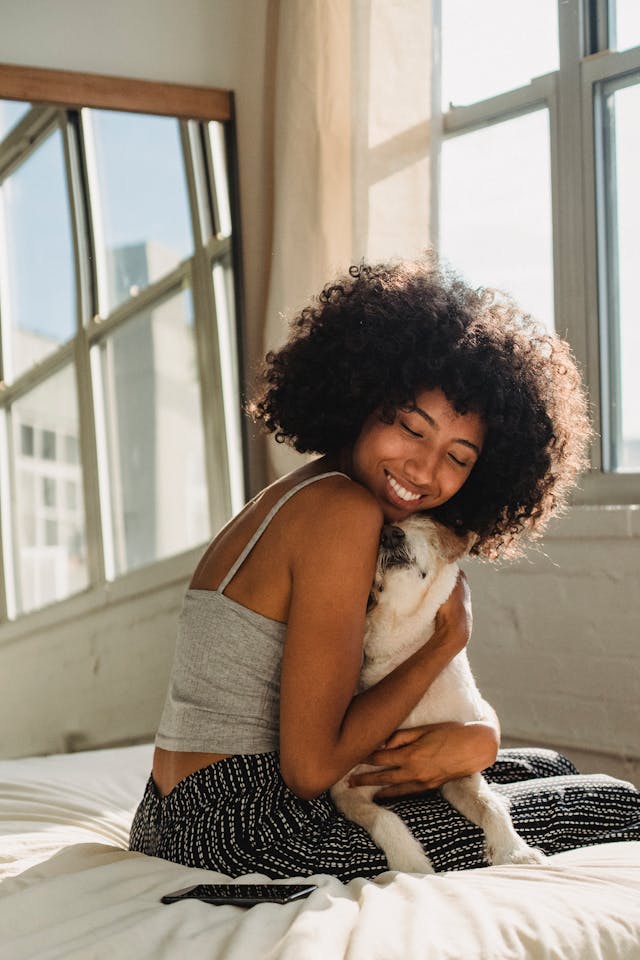 ベッドで微笑みながら愛犬を抱きしめる女性。