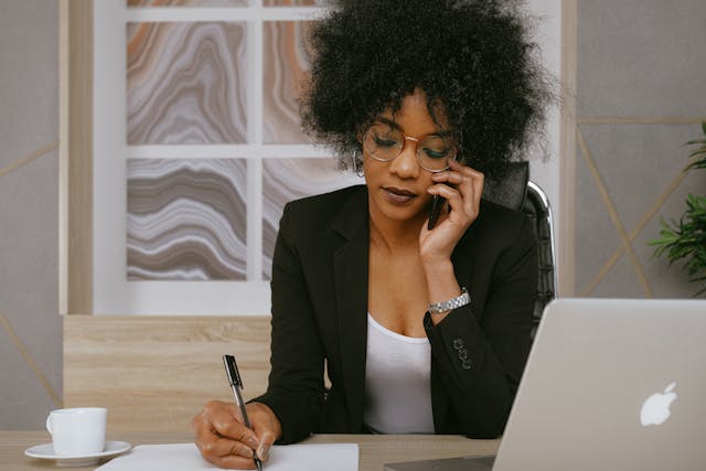 Une femme d'affaires parle au téléphone tout en prenant des notes avec un stylo et du papier.